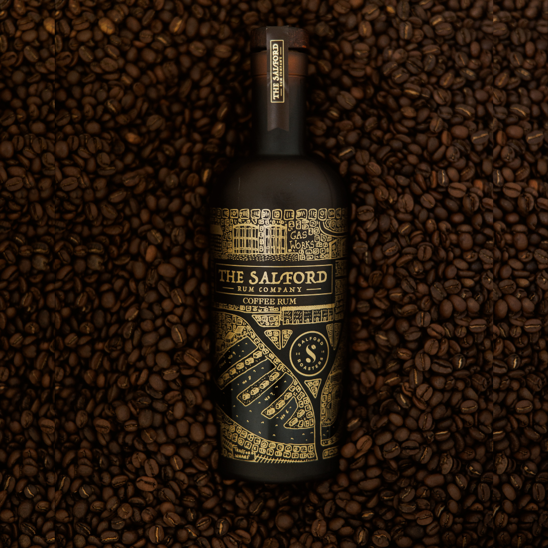Salford Coffee Rum 70cl bottle laying on a bed of roasted coffee beans showing the gold map design.