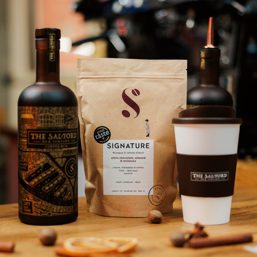 Salford Coffee Rum bottle next to a bag of Salford Roasters signature coffee beans and a takeaway coffee cup.